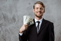 Young successful businessman smiling, holding money over grey background. Royalty Free Stock Photo