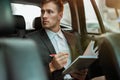 Young successful businessman takes notes to his planner while sitting in his car on the way to meetting with partners, Royalty Free Stock Photo