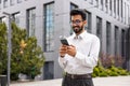 Young successful businessman walking down the street holding a phone in his hands, an Indian man using an application on Royalty Free Stock Photo