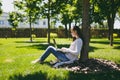 Young successful businesswoman in casual clothes. Woman sit on grass ground, working on laptop pc computer in city park Royalty Free Stock Photo