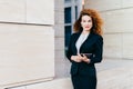 Young successful businesswoman in elegant clothes, having luxuriant hair, holding tablet in hands while going for work. Gorgeous f Royalty Free Stock Photo