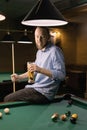 Young successful handsome man playing in pool at bar drinking beer while sitting on the table Royalty Free Stock Photo