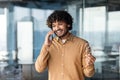 Young successful hispanic businessman in a shirt talking on the phone inside the office, man standing near the window Royalty Free Stock Photo