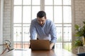 Young successful male manager leaning over table writing email.