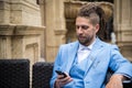 Young successful man in a blue suit looking at a smartphone while sitting in a luxury street cafe Royalty Free Stock Photo