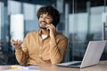 Young successful man working inside office on laptop at workplace, businessman in shirt talking cheerfully smiling on Royalty Free Stock Photo