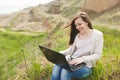 Young successful pretty smart business woman or student in light casual clothes sitting on grass using laptop in field Royalty Free Stock Photo