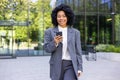 Young successful satisfied business woman walking with phone in hands, African American woman in business suit with Royalty Free Stock Photo