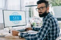 young successful seo manager sitting at workplace with computer and looking Royalty Free Stock Photo