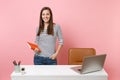 Young successful woman in casual clothes holding notebook work standing near white desk with contemporary pc laptop Royalty Free Stock Photo