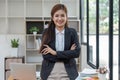 Young successful woman entrepreneur or an office worker stands with crossed arms near a desk in a modern office, looking Royalty Free Stock Photo