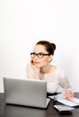 Young successful woman entrepreneur wearing eyeglasses sits at her desk on a white background at her laptop, holds her mobile Royalty Free Stock Photo