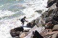 Young surfer with surf board goes out of water to the rude rock coast on a bay in San Francisco