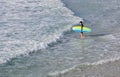 Young surfer walks into the water to confront the surf by surfing the rougher waters after a morning rain storm