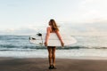 Young surfer woman holding white short surfboard on a beach at sunset or sunrise. Royalty Free Stock Photo