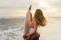 Young surfer woman holding white short surfboard on a beach at sunset or sunrise. Royalty Free Stock Photo