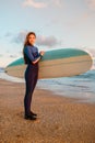 Young surfer woman with surfboard on a beach at warm sunset or sunrise. Royalty Free Stock Photo