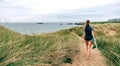 Surfer woman with wetsuit and surfboard walking along the path between the dunes towards the beach Royalty Free Stock Photo