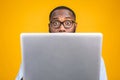 Young surprised african american man standing and using laptop computer isolated over yellow background Royalty Free Stock Photo