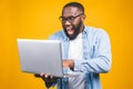 Young surprised african american man standing and using laptop computer isolated over yellow background Royalty Free Stock Photo