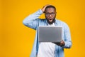 Young surprised african man standing and using laptop computer isolated over yellow background Royalty Free Stock Photo