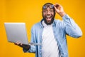 Young Surprised African Man Standing And Using Laptop Computer Isolated Over Yellow Background