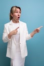 young surprised blondie elegant female adult wearing jacket and dress points finger to the side