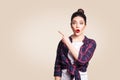 Young surprised girl with casual style and bun hair pointing her finger sideways, demonstrating something on beige blank wall Royalty Free Stock Photo