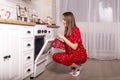 Young surprised and glad woman checking oven in kitchen and looking if bakery is ready. Female at home in pyjamas at christmas eve Royalty Free Stock Photo