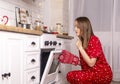 Young surprised and glad woman checking oven in kitchen and looking if bakery is ready. Female at home in pyjamas at christmas eve Royalty Free Stock Photo