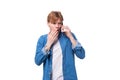 young surprised guy with red hair in a denim shirt speaks on the phone in secret Royalty Free Stock Photo