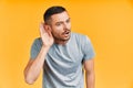 Young surprised man listening something carefully and holds his hand near ear over yellow background Royalty Free Stock Photo