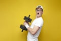 Young surprised nerd guy in glasses holds heavy dumbbells and angrily shouts on a yellow background