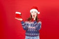 young surprised woman with gift Shoe in her hand in a sweater with snowflakes and a Santa Claus hat on a red background Royalty Free Stock Photo