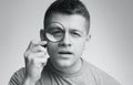 Young suspicious man looking at camera through magnifier