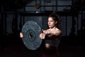 Young sweaty muscular strong fit girl holding big heavy barbell weight plate with her hands and lifting it up as hardcore cross wo Royalty Free Stock Photo