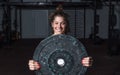 Young sweaty muscular strong fit girl holding big heavy barbell weight plate with her hands and lifting it up as hardcore cross wo Royalty Free Stock Photo