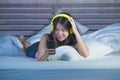 Young sweet and happy Asian Chinese 20s woman listening to music song with headphones headset and mobile phone lying in bed relaxe