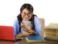 Young sweet and happy Asian Chinese student girl in nerd glasses working cheerful on laptop computer on desk with pile of books Royalty Free Stock Photo