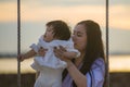 Young sweet and happy Asian Chinese woman holding baby girl swinging together at beach swing on Summer sunset in mother and little Royalty Free Stock Photo