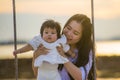 Young sweet and happy Asian Chinese woman holding baby girl swinging together at beach swing on Summer sunset in mother and little Royalty Free Stock Photo