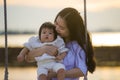 Young sweet and happy Asian Chinese woman holding baby girl swinging together at beach swing on Summer sunset in mother and little Royalty Free Stock Photo