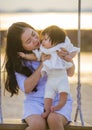 Young sweet and happy Asian Chinese woman holding baby girl swinging together at beach swing on Summer sunset in mother and little Royalty Free Stock Photo