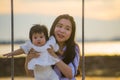 Young sweet and happy Asian Chinese woman holding baby girl swinging together at beach swing on Summer sunset in mother and little Royalty Free Stock Photo