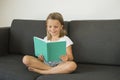 Young sweet and happy little girl 6 or 7 years old sitting on home living room sofa couch reading a book quiet and adorable in chi Royalty Free Stock Photo