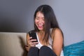 Young sweet happy and pretty Asian Korean woman using internet social media app on mobile phone laughing cheerful having fun at ho Royalty Free Stock Photo