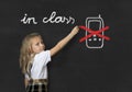 Young sweet junior schoolgirl writing with chalk about not using mobile phone in school class Royalty Free Stock Photo