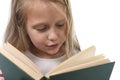 Young sweet little 6 or 7 years old with blond hair girl reading a book looking curious and fascinated Royalty Free Stock Photo