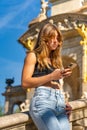 Young, tanned, beautiful woman in a black top and jeans and long hair looking, reading, typing on her mobile phone leaning against Royalty Free Stock Photo