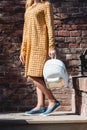 Young tanned woman standing on the stone stairs. Woman in a yellow dress and blue shoes with white backpack in hands. Royalty Free Stock Photo